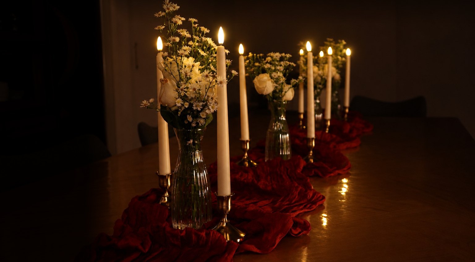 A candlelit table with a red runner, LED taper candles in gold holders, clear acrylic vases and ivory flowers