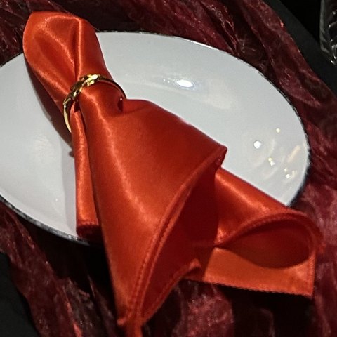 Red satin napkin with a gold napkin ring on a white plate