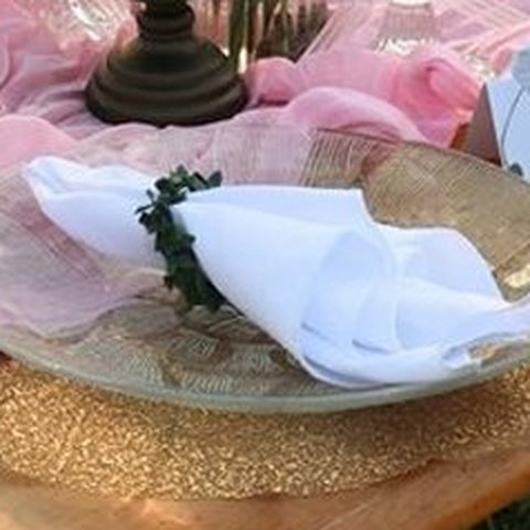 White cloth napkin with a leaf napkin ring on a gold-rimmed plate
